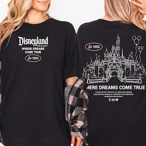 May include: Black t-shirt featuring the Disneyland Resort logo and the text "WHERE DREAMS COME TRUE" with "Est. 1955". The back of the shirt displays a castle graphic and the words "HERE DREAMS COME TRUE".