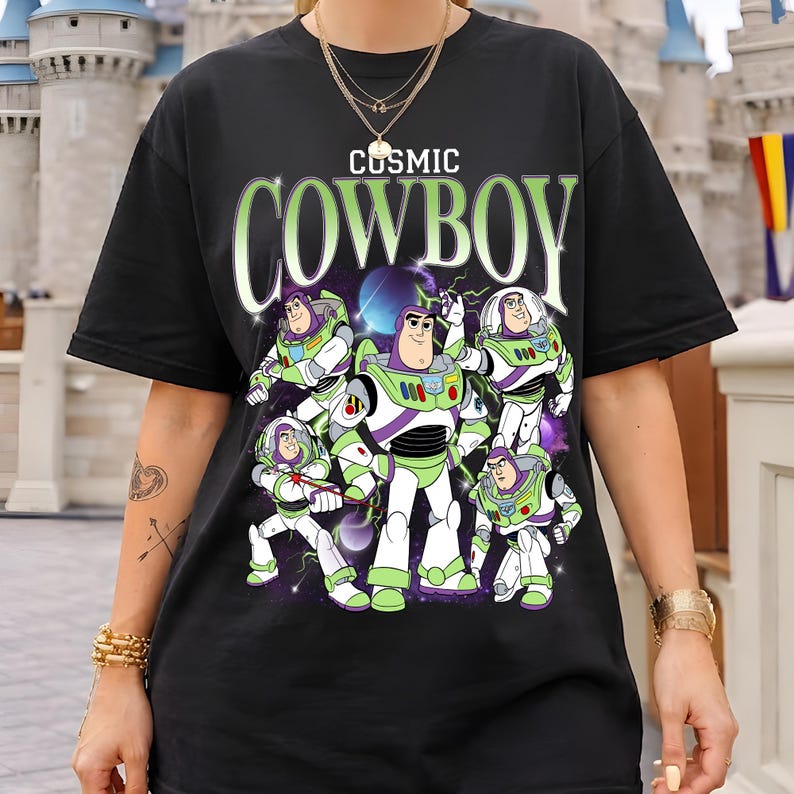 May include: A black short-sleeve t-shirt featuring a graphic print of multiple Buzz Lightyear characters in various poses against a cosmic background. The text "COSMIC COWBOY" is printed in large, light green letters above the character illustrations.