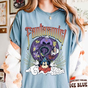 May include: Ice blue t-shirt with the word "Fantasmic!" in a retro font. The shirt features a graphic of Mickey Mouse as the Sorcerer's Apprentice, surrounded by Disney villains. The shirt is labeled "Comfort Color Ice Blue."