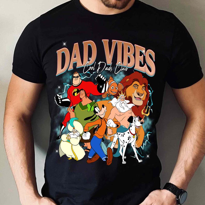 Puede incluir: Camiseta negra con un gr&aacute;fico de personajes de dibujos animados, incluyendo Los Incre&iacute;bles, Nemo, Simba y otros. El texto "DAD VIBES Cool Dads Club" est&aacute; impreso sobre los personajes en un estilo retro.