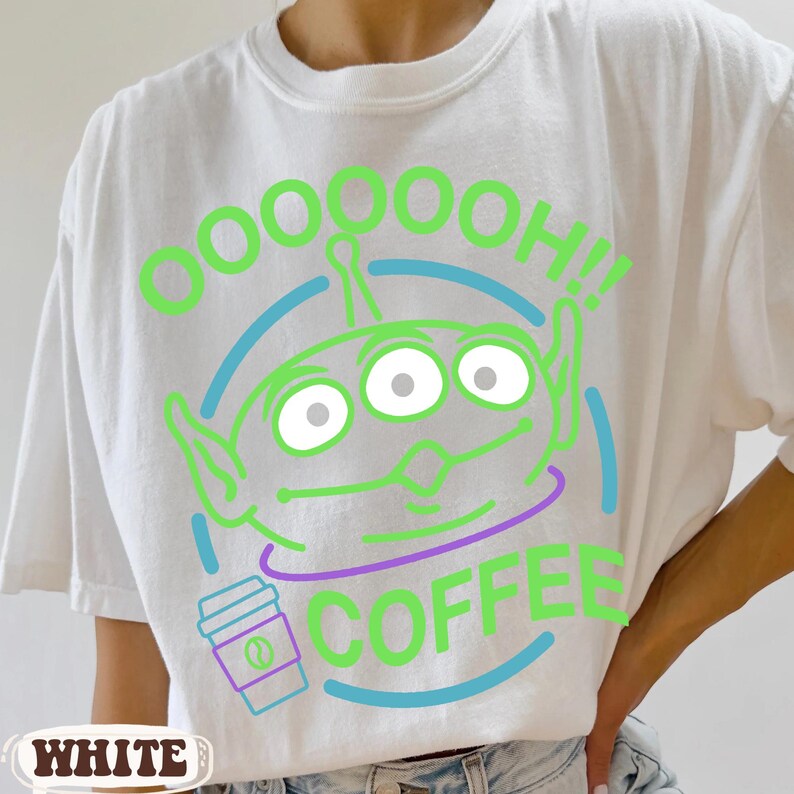 Puede incluir: Camiseta blanca con un dise&ntilde;o de alien&iacute;gena verde de dibujos animados y el texto "OOOOOH!! COFFEE". El dise&ntilde;o incluye un gr&aacute;fico de taza de caf&eacute;. La camiseta es de estilo casual.