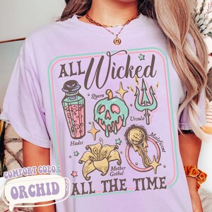 May include: A light purple t-shirt with the words "ALL Wicked ALL THE TIME" and various cartoon illustrations of villains. The shirt also has the words "COMFORT COLOR" and "ORCHID" printed on it.