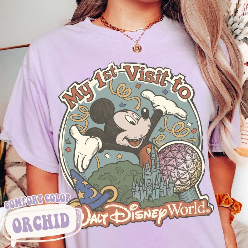 May include: Orchid-colored t-shirt with a graphic featuring Mickey Mouse, the text "My 1st Visit to Walt Disney World," and iconic park imagery. The shirt has a comfort color and a relaxed fit.