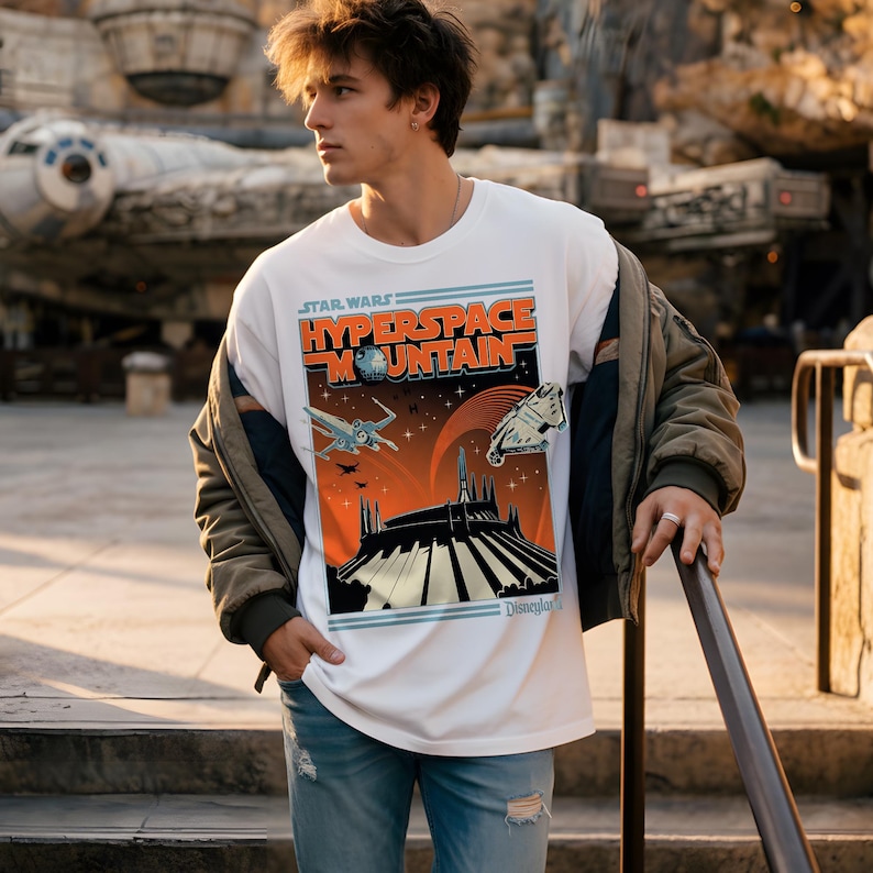 May include: White t-shirt featuring a Star Wars Hyperspace Mountain graphic. The design includes an orange and black mountain scene with spaceships and the text "Star Wars Hyperspace Mountain". The shirt is a classic crew neck.