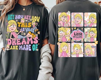 May include: Dark gray t-shirt featuring a colorful graphic design. The front of the shirt displays the text "HEY NOW HEY NOW THIS IS WHAT DREAMS ARE MADE OF" with a cartoon illustration. The back has a grid of cartoon images and the text "Lizzie McGuire".