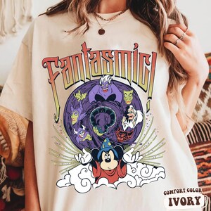 May include: Ivory-colored t-shirt featuring the word "Fantasmic!" in a retro font. The graphic includes Disney villains and Mickey Mouse as the Sorcerer's Apprentice. The shirt is labeled "Comfort Color Ivory".