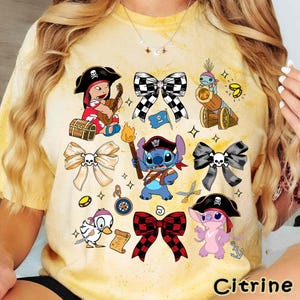 Może przedstawiać: Ż&oacute;łta koszulka tie-dye z r&oacute;żnymi postaciami pirat&oacute;w z kresk&oacute;wek i kokardami z motywem czaszki. Projekt zawiera piracką dziewczynę grającą na gitarze, Stitcha jako pirata i słowo "Citrine" na dole.