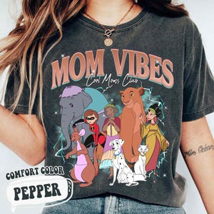 May include: A gray t-shirt with the text "Mom Vibes Cool Moms Club" in pink and blue. The shirt features a graphic of Disney characters including Dumbo,  the  lion from The Lion King,  and  the  dalmatian from 101 Dalmatians.