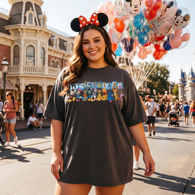 Puede incluir: Una camiseta gris oscuro con un gr&aacute;fico colorido de personajes de Disney. La persona lleva una diadema de orejas de Minnie Mouse con un lazo rojo y sostiene un mont&oacute;n de globos de Mickey Mouse. El fondo muestra un parque tem&aacute;tico.