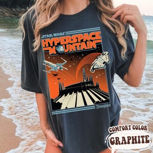 May include: Dark gray t-shirt featuring a Star Wars Hyperspace Mountain design. The graphic includes spaceships, a planet, and the Disneyland logo. The shirt is labeled "Comfort Color Graphite."