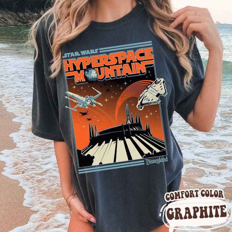 May include: Dark gray t-shirt featuring a Star Wars Hyperspace Mountain design. The graphic includes spaceships, a planet, and the Disneyland logo. The shirt is labeled "Comfort Color Graphite."