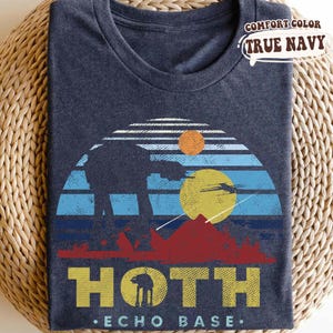 May include: True navy blue t-shirt with a graphic design featuring a sunset scene with an AT-AT walker, mountains, and the text "HOTH - ECHO BASE." The shirt is labeled "COMFORT COLOR."