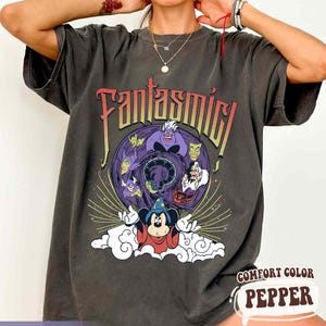 May include: Dark gray t-shirt featuring a colorful graphic from Fantasmic. The design includes Mickey Mouse in a sorcerer's outfit, surrounded by various Disney villains. The text "Fantasmic" is displayed above the graphic.