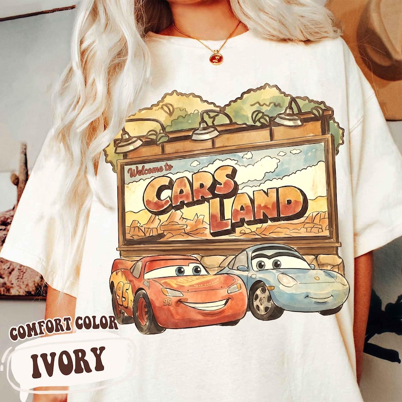 Op de afbeelding: Ivoorkleurig T-shirt met een Cars Land-afbeelding. Het ontwerp bevat een bord met de tekst "Welcome to Cars Land" en illustraties van Bliksem McQueen en Sally Carrera. Het shirt is een comfortkleur.