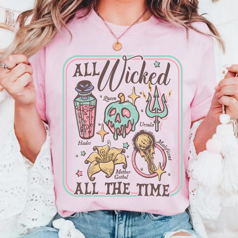 May include: Pink t-shirt with the text "ALL Wicked ALL THE TIME" in a rectangular design. The design includes illustrations of a potion bottle, a skull, a trident, a flower, and a golden orb, with character names.
