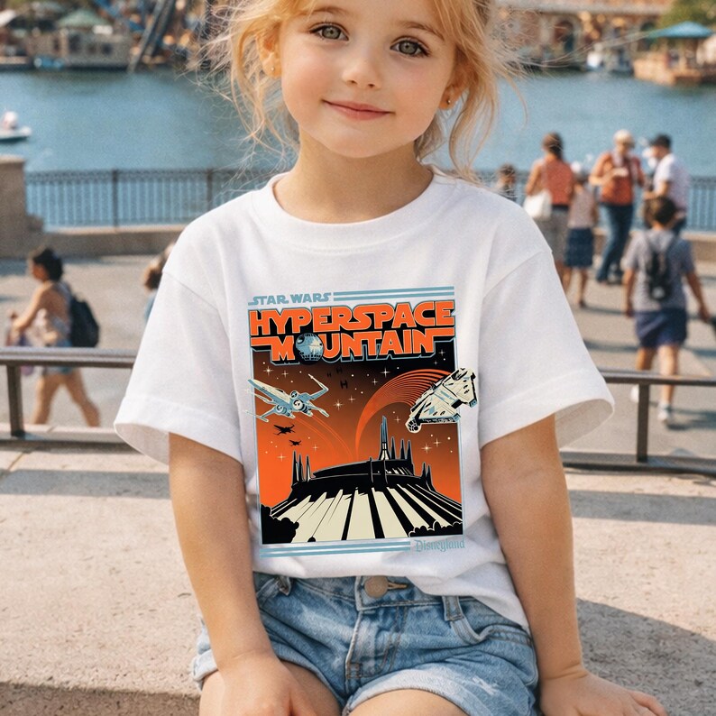 May include: White t-shirt featuring a Star Wars Hyperspace Mountain graphic. The design includes spaceships, a mountain silhouette, and the Disneyland logo. The shirt is worn by a young person.