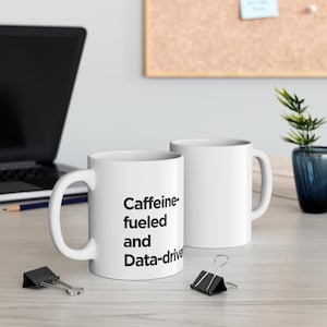 Peut inclure: Deux tasses en céramique blanche avec du texte noir. La tasse de gauche dit "Caffeine-fueled and Data-driven".