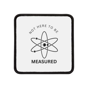 May include: White patch with black text and an atom symbol. The text reads "Not here to be measured".