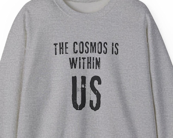 Puede incluir: Sudadera gris con el texto "THE COSMOS IS WITHIN US" y "CARL SAGAN" impreso en la parte delantera.