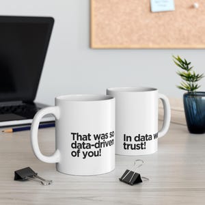 Può includere: Due tazze in ceramica bianca con testo nero. Una tazza recita "That was so data-driven of you!" e l'altra dice "In data we trust!". Le tazze sono su una superficie di colore chiaro.