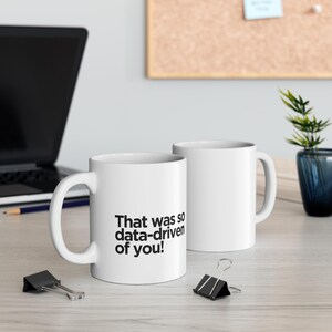 Peut inclure: Deux tasses en céramique blanche avec du texte noir. La tasse de gauche dit "That was so data-driven of you!"