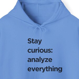 Puede incluir: Una sudadera con capucha azul claro con el texto "Stay curious: analyze everything" impreso en negro.