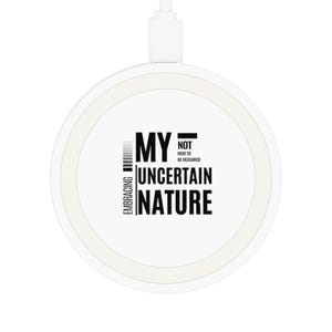 May include: A white wireless charger with the text "MY UNCERTAIN NATURE" in black. The charger also has the words "EMBRACING" and "NOT HERE TO BE MEASURED" in black. A white USB cable is attached to the charger.