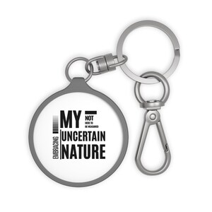 May include: A silver keyring with a round, grey charm that says "Embracing My Uncertain Nature - Not Here To Be Measured".