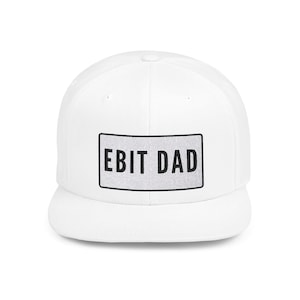May include: White baseball cap with a flat peak. The cap displays the text "EBIT DAD" in black block letters on a rectangular patch. The patch has a silver glittery background and a black border.