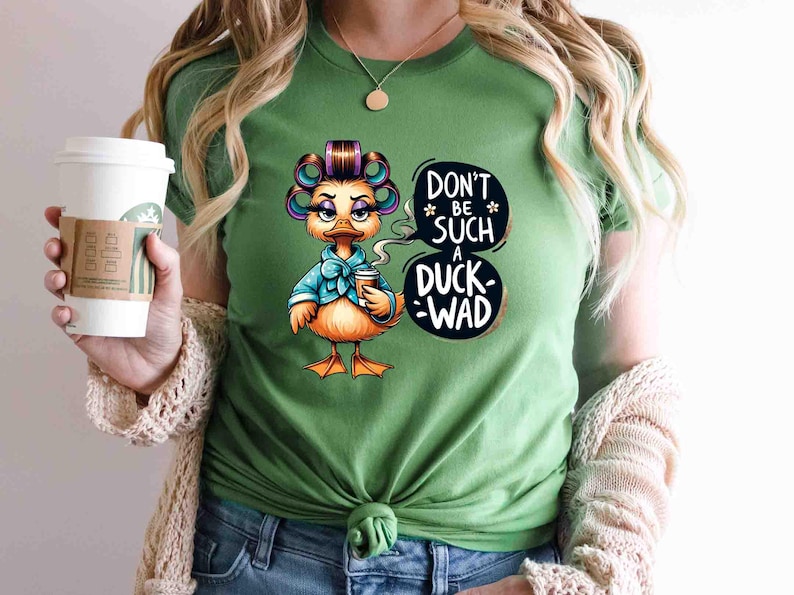 May include: Green t-shirt featuring a cartoon duck with curlers, a blue bow, and a coffee cup. The duck is saying "Don't be such a duck-wad" in a speech bubble. The shirt is a solid green color.