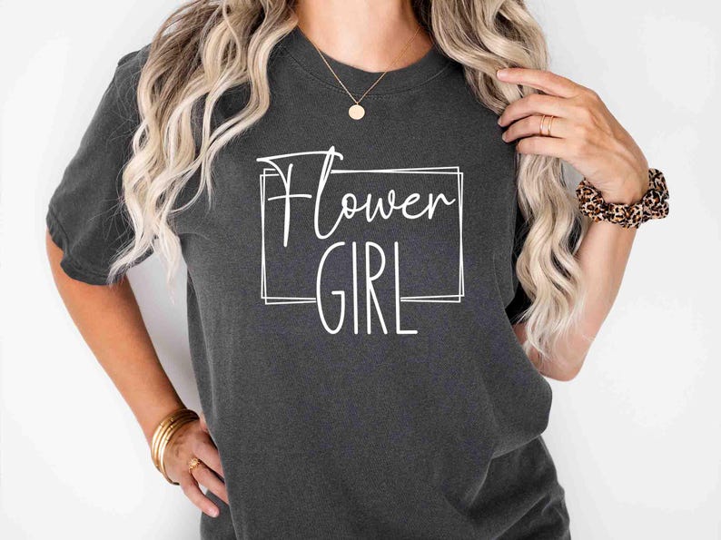 K&ouml;nnte beinhalten: Dunkelgraues T-Shirt mit dem wei&szlig;en Schriftzug "Flower Girl" in einem wei&szlig;en rechteckigen Rahmen. Das Shirt hat kurze &Auml;rmel und einen Rundhalsausschnitt. Der Stil ist l&auml;ssig und entspannt.