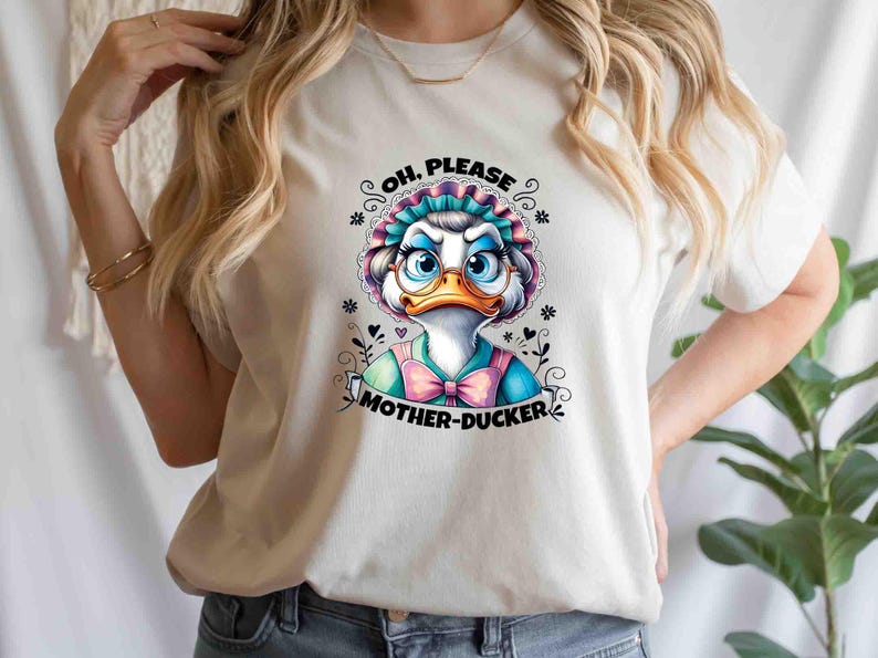 May include: White t-shirt featuring a cartoon duck wearing glasses and a bonnet. The duck has a blue and pink bow tie and the text "OH, PLEASE MOTHER-DUCKER" is printed below the duck image. The shirt is a casual style.