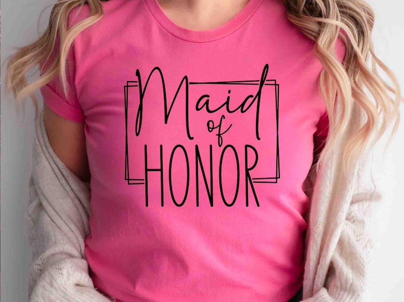 K&ouml;nnte beinhalten: Ein leuchtend pinkfarbenes T-Shirt mit dem schwarzen Schriftzug "Maid of Honor" in einem schwarzen rechteckigen Rahmen. Das T-Shirt hat kurze &Auml;rmel und wird von einer Person mit blonden Haaren getragen.