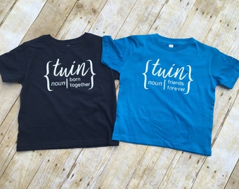 May include: Two t-shirts with the word "twin" in curly brackets. The black t-shirt says "twin noun | born together". The blue t-shirt says "twin noun | friends forever".