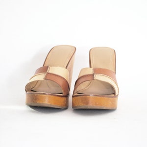 May include: A pair of brown and beige wedge sandals with a cork platform.