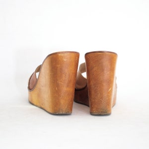 May include: A pair of brown leather wedge sandals with a thick wooden platform sole.