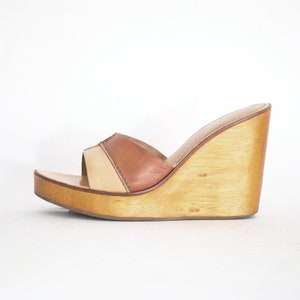 May include: A pair of brown and beige leather wedge sandals with a wooden platform sole.