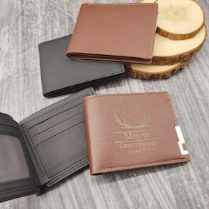 May include: Three brown leather wallets with a gold accent. One wallet has the text "Meyer,  Groomsman, 10.26.2022" and a deer antler design.