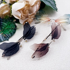 May include: Three pairs of butterfly-shaped sunglasses with translucent wings. The sunglasses are in black, brown, and rainbow colors.