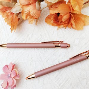 Puede incluir: Dos bolígrafos de color oro rosa con acabado metálico. Un bolígrafo tiene la palabra "Simon" grabada en el lateral.