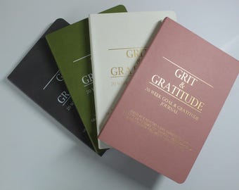 May include: Four journals in shades of gray, green, white, and pink are fanned out. The pink journal is in the foreground and has the words "GRIT & GRATITUDE" in gold lettering. The journals are for a 20-week goal and gratitude journal.