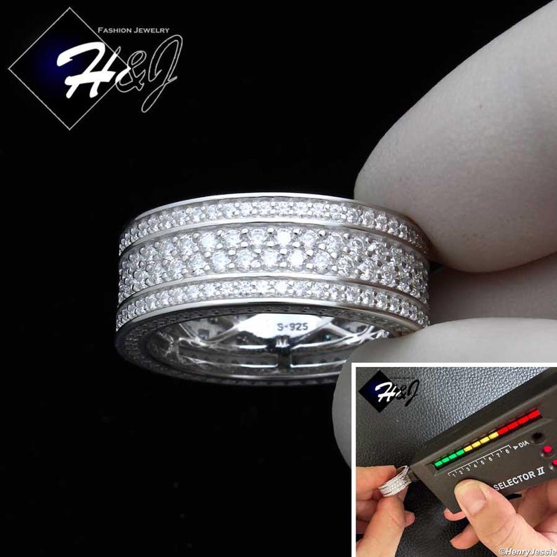 May include: A silver ring with multiple rows of small, clear gemstones. The ring is held by a gloved hand, with a diamond tester in the background. The ring is marked with "S-925". The image also includes the text "FASHION JEWELRY" and the logo "H&J".