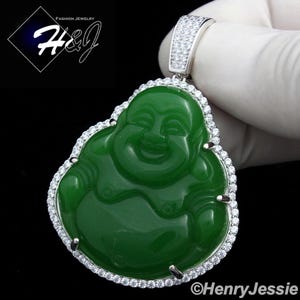 May include: A green jade Buddha pendant with a silver bail and a halo of small, clear stones. The pendant has a smiling Buddha figure carved into the jade. The jewelry is set against a black background.