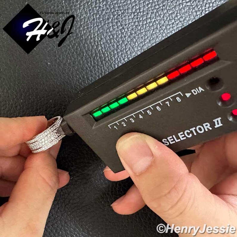 May include: A silver ring with multiple rows of small, clear stones is being tested with a diamond tester. The tester displays a green light, indicating the ring's authenticity. The image includes the text "H&J Fashion Jewelry" and "Henry Jessie".