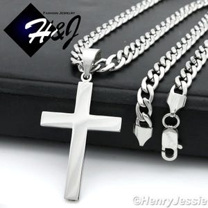 May include: A silver chain necklace with a large silver cross pendant. The chain is a curb style and the cross is flat and smooth.