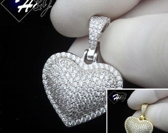 May include: A silver-colored heart-shaped pendant encrusted with numerous small, clear gemstones. The pendant is held against a dark background, with a smaller gold-colored version in the corner. The text "Fashion Jewelry" and the logo "H&J" are visible.