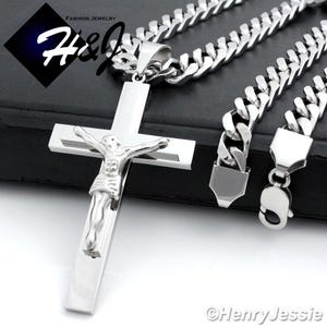 May include: A silver-colored necklace featuring a large cross pendant with a detailed depiction of Jesus Christ. The cross hangs from a thick, silver chain. The image includes the text "FASHION JEWELRY" and the brand name "H&J".