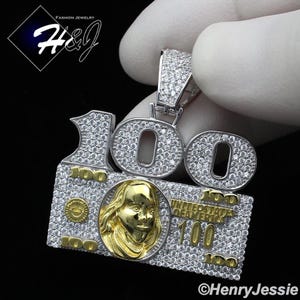 May include: Silver pendant featuring a $100 bill design with a large '100' in the center, surrounded by smaller '100's and a portrait of Benjamin Franklin. The pendant is covered in clear cubic zirconia stones.