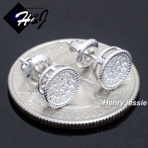 May include: A pair of silver stud earrings with a round, pave-set diamond design. The earrings are shown on a US quarter for size reference.