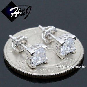 May include: A pair of silver stud earrings with a square-shaped clear cubic zirconia stone in the center of each earring. The earrings are shown on a US quarter for size reference.